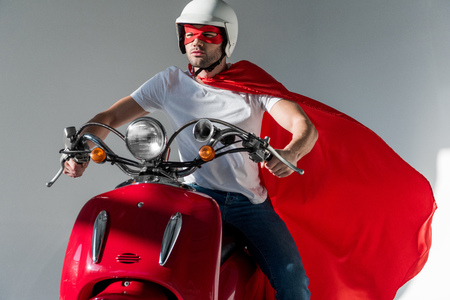 man in protective helmet and superhero costume riding red scooterの写真素材