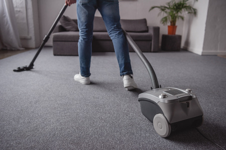 cropped image of man cleaning carpet with vacuum cleaner in living roomの写真素材