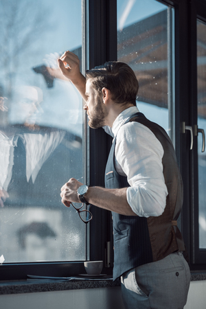 portrait of stylish young businessman holding eyeglasses and looking at windowの写真素材