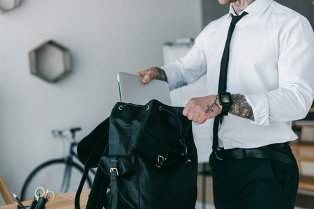 cropped shot of young tattooed businessman putting laptop into backpackの写真素材