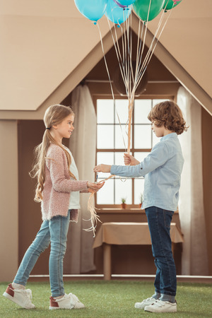 kid presenting balloons to beautiful little girlfriend in front of cardboard houseの写真素材