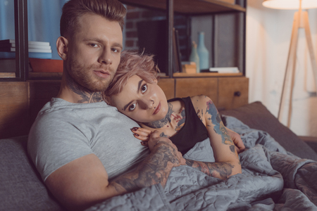 beautiful tattooed couple relaxing on bed at homeの写真素材