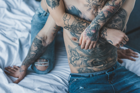 cropped view of girlfriend embracing her tattooed boyfriend in bedの写真素材