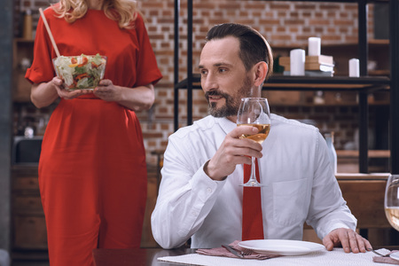 cropped image of wife serving table with appetizing salad and husband drinking wine at romantic dinnerの写真素材
