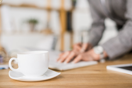 selective focus of cup of coffee on table with businesswoman making notesの写真素材