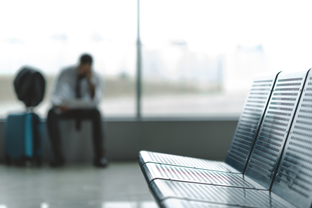 close-up shot of seats at airport lobby with buisnessman waiting for plane blurred on backgroundの写真素材