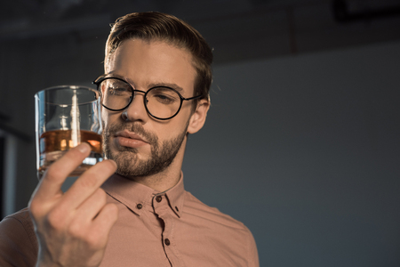 close-up view of stylish young man in spectacles holding glass of whiskyの写真素材
