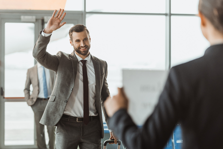 businessman waving to partner who waiting for him with name sign on paper at airportの写真素材