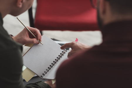 cropped image of man pointing on something in friends notebook in libraryの写真素材