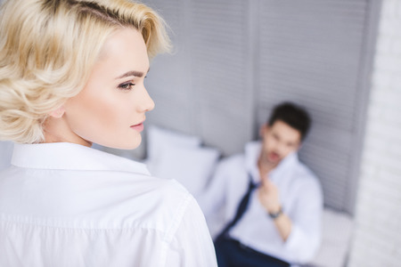 beautiful blonde girl looking away while boyfriend lying on bedの写真素材