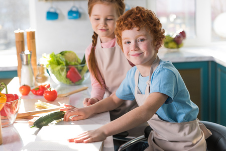 beautiful happy children in aprons cooking together in kitchenの写真素材