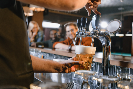 cropped image of barman pouring beer in glass at barの写真素材