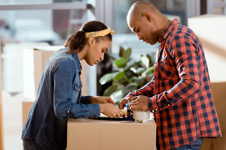 african american couple packing cardboard box with scotch tapeの写真素材