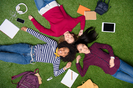 overhead view of cheerful multicultural students lying on green lawnの写真素材