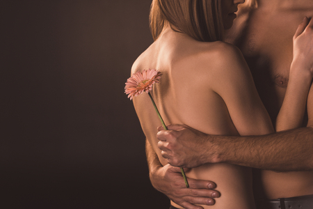 cropped view of tender couple hugging and holding flower, isolated on brownの写真素材