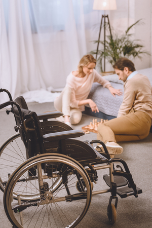 husband with disability and wife playing chess in bedroom with wheelchair on foregroundの写真素材