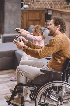 happy daughter and father on wheelchair playing video game with joysticksの写真素材