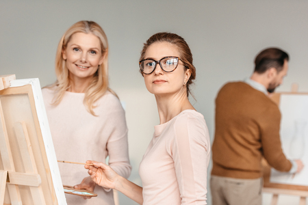 beautiful middle aged women looking at camera while painting together at art classの写真素材