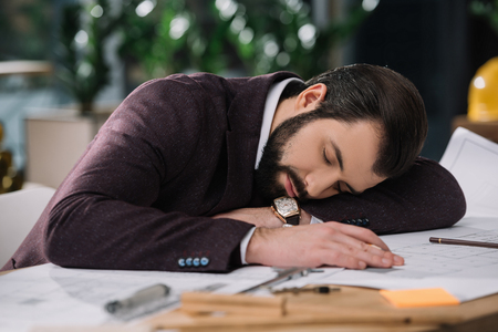 exhausted architect sleeping on building plans at workplaceの写真素材