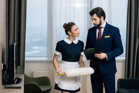 hotel administrator with clipboard talking to maid with duster at suiteの写真素材