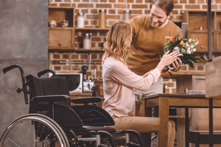 smiling man presenting flowers to disabled wife at homeの写真素材