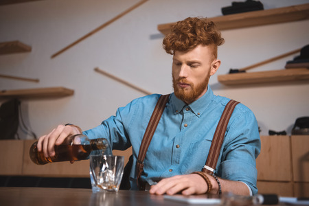 handsome stylish young man pouring whisky from bottle in glassの写真素材