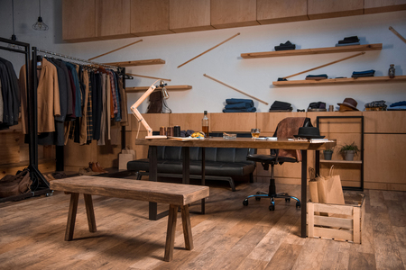 clothing design studio interior with stylish clothes on hangers and bottle of whisky on tableの写真素材