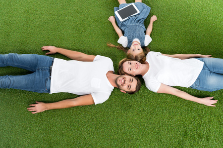overhead view of family with digital tablet lying on green grassの写真素材