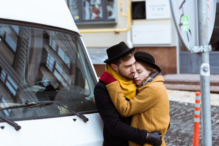 beautiful young couple hugging in autumn outfit beside carの写真素材
