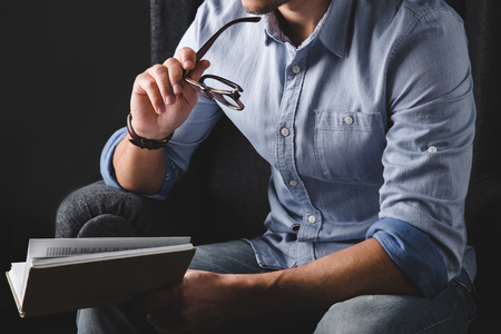 cropped view of man holding eyeglasses while reading bookの写真素材
