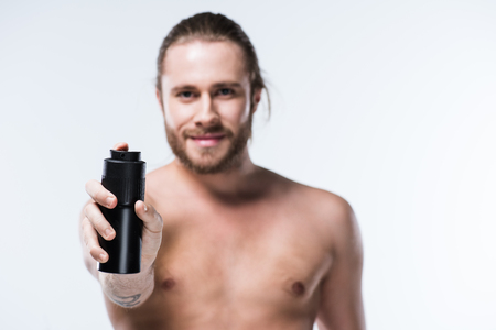 Cheerful young man holding deodorant spray in outstretched handの写真素材