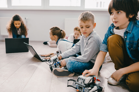 focused kids programming robots with laptops while sitting on floor, stem education conceptの写真素材