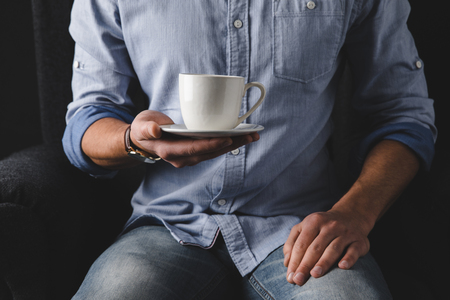 cropped view of man in shirt holding cup of coffeeの写真素材