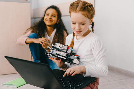 teen schoolgirls programming robot while sitting on floorの写真素材