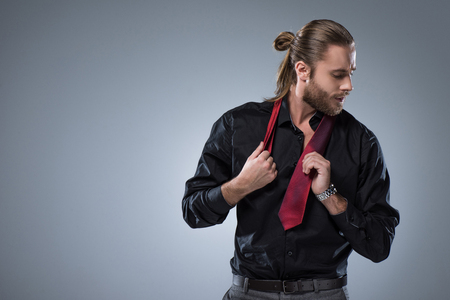 Young  bearded man in black shirt with red tie around his neck,  isolated on grayの写真素材