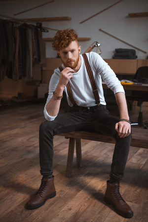 full length view of handsome stylish young male fashion designer sitting and looking at cameraの写真素材