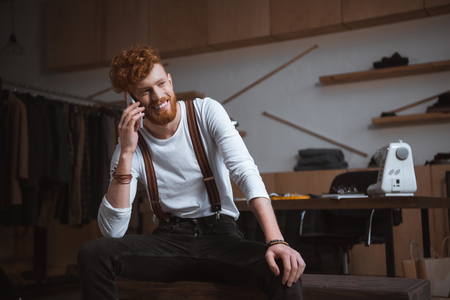 handsome young smiling fashion designer talking by smartphone at workplaceの写真素材
