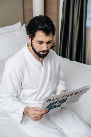 serious businessman in bathrobe reading newspaper at hotel suiteの写真素材