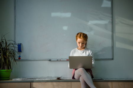 concentrated little child working with laptop in front of whiteboardの写真素材