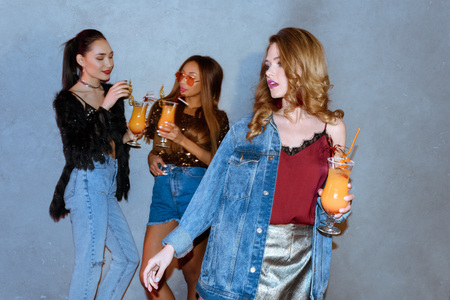 fashionable girl holding glass with cocktail while multiethnic friends standing behindの写真素材
