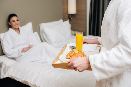 cropped shot of man carrying tray with breakfast for girlfriend while she sitting in bed at hotel suiteの写真素材