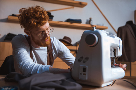 focused young fashion designer in eyeglasses working with sewing machineの写真素材