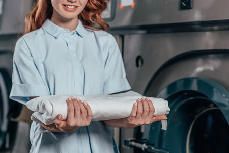 cropped shot of female dry cleaning worker holding stack of clean white clothesの写真素材