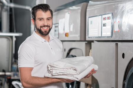 happy dry cleaning worker holding stack of clean clothesの写真素材
