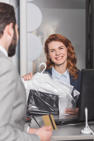 dry cleaning manageress standing at workplace with bag of clothes while customer holding gold credit cardの写真素材