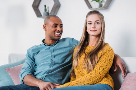 multicultural couple holding hands on sofaの写真素材