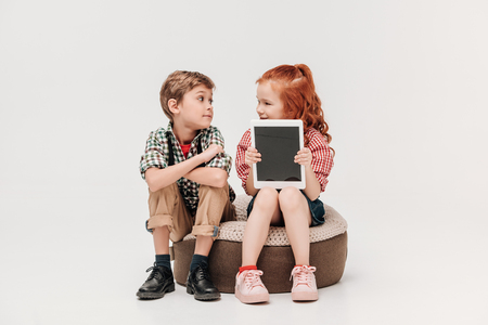 beautiful kids looking at each other and showing digital tablet with blank screen isolated on greyの写真素材