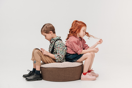 children sitting back to back while boy using digital tablet isolated on greyの写真素材