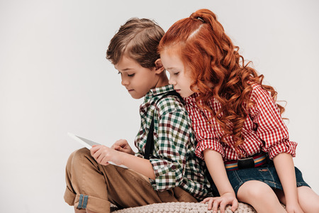 beautiful little child looking at friend using digital tablet isolated on greyの写真素材