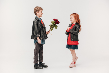 boy presenting roses bouquet to his beautiful little girlfriend isolated on greyの写真素材